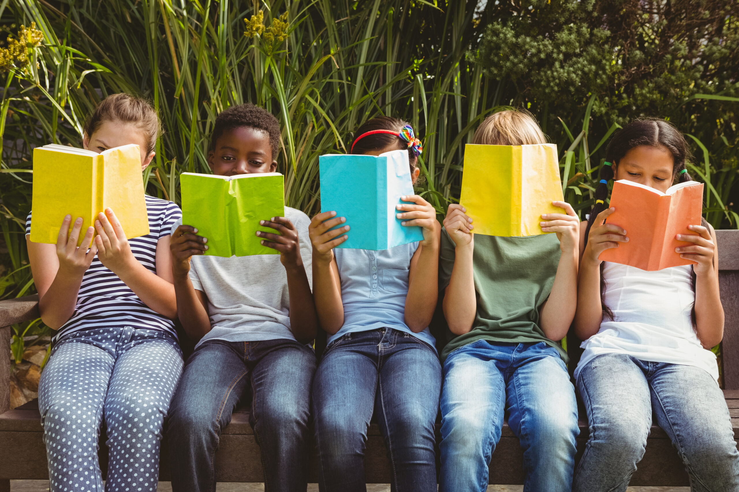 Children sitting in row and reading books at the park