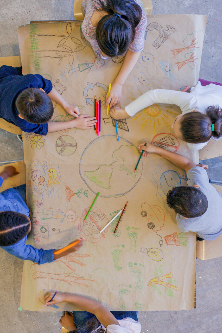 An aerial view of a multi ethnic group of children learn about going green and color in environmentally friendly concepts surrounding a drawing of Earth.